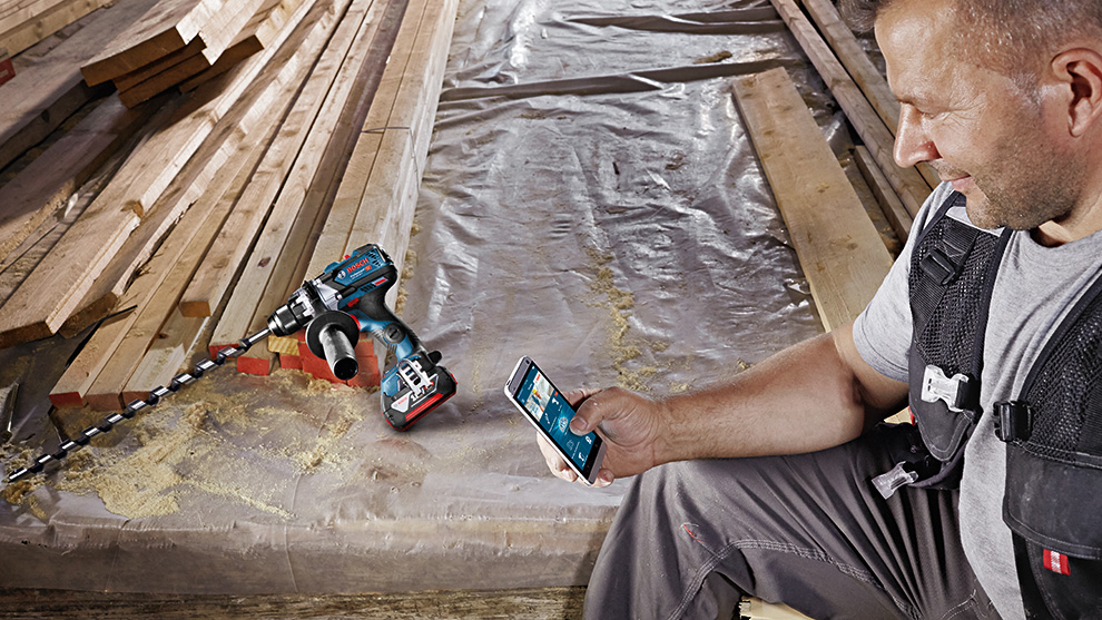 Une perceuse-visseuse sans fil Bosch Professional est posée sur du film, un homme regarde son téléphone.