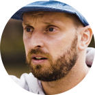 Un uomo con la barba indossa un cappello blu e guarda seriamente.