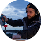 Un uomo con le cuffie sta tagliando legno con una sega Bosch all'aperto.