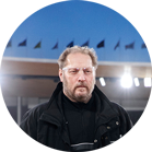 Un uomo con barba e giacca nera sta sotto i riflettori.