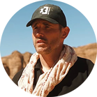 Un uomo con un cappello nero e una sciarpa sta davanti a un paesaggio roccioso.