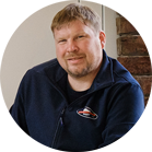 Un uomo sorridente con i capelli corti indossa un maglione blu.