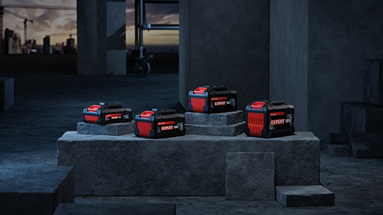 Five Bosch Professional battery packs on gray stones, dark surroundings.