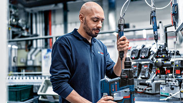 Un uomo testa un avvitatore a batteria blu Bosch Professional in un'officina.