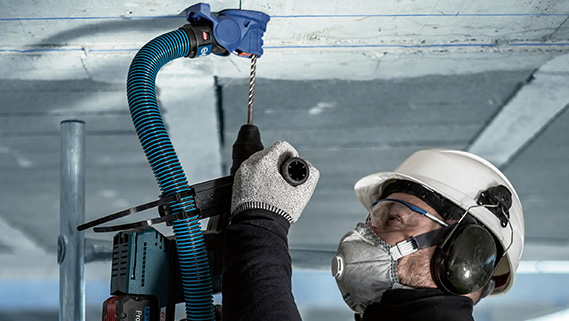 En håndverker med hjelm og hørselvern borer i taket.