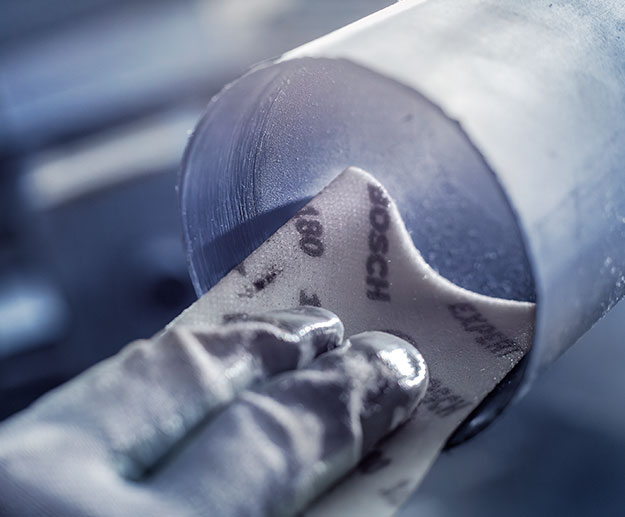 En hånd holder Bosch sandpapir mot et rundt metallstykke.