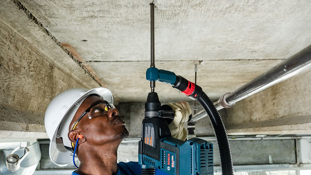 A worker wearing a helmet operates a Bosch Professional drill on the ceiling.