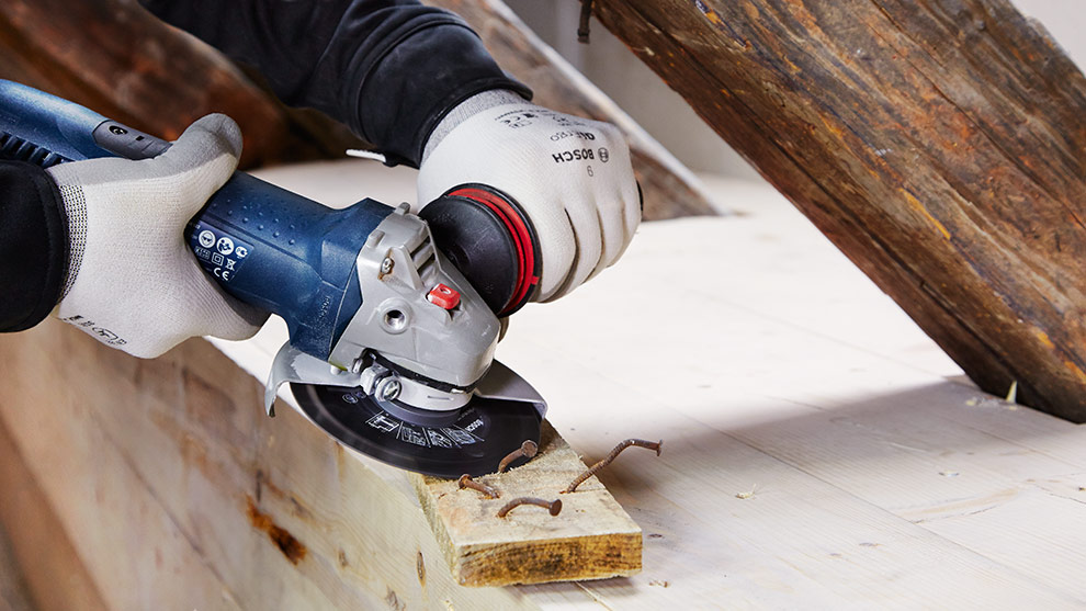 A person is cutting wood with a blue Bosch angle grinder.