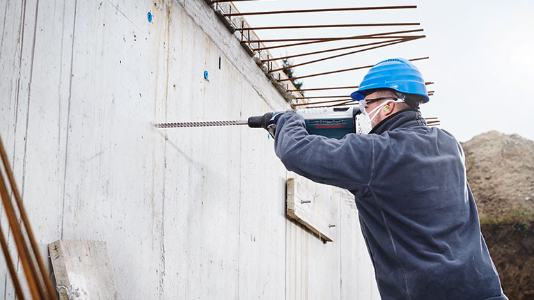 Vakman met een blauwe helm boort in een betonnen muur.