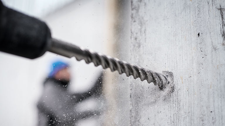 Een Bosch Professional boor dringt door een grijze muur, stof vliegt op.