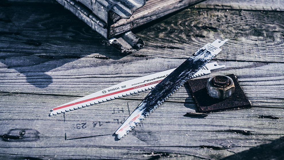 Due lame di sega Bosch sono appoggiate su un tavoletta di legno accanto a una vite.