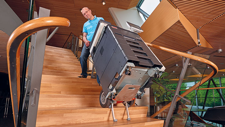 Muž nese černý nářaďový kufr Bosch dolů po schodech.