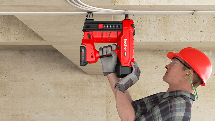 Muž s červenou helmou používá červenou akumulátorovou hřebíkovačku.