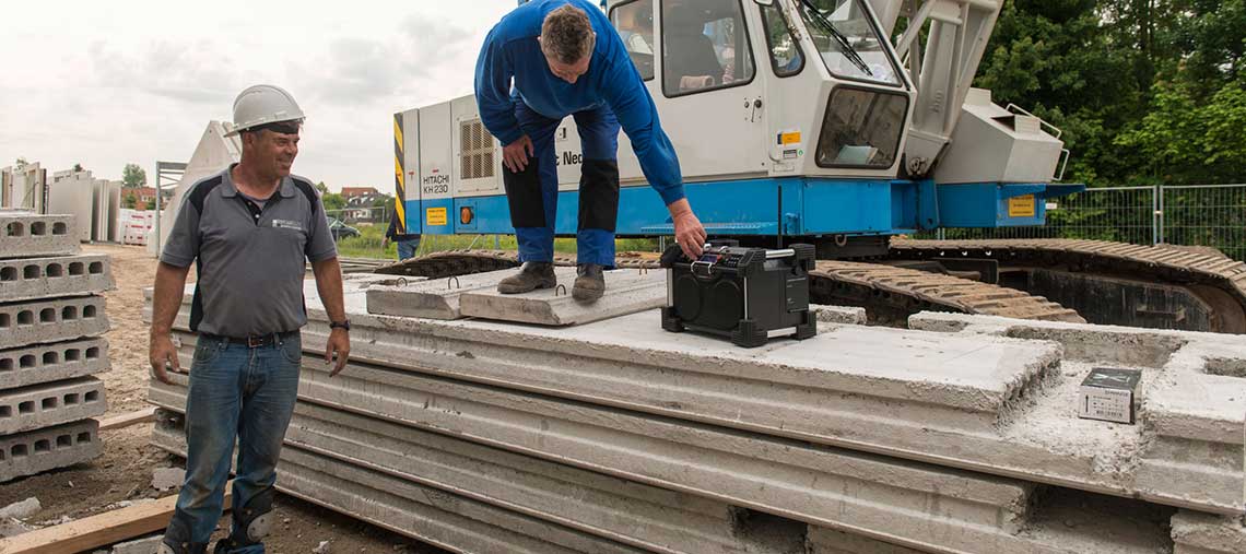 Dva stavební dělníci stojí vedle betonových desek a jeřábu.