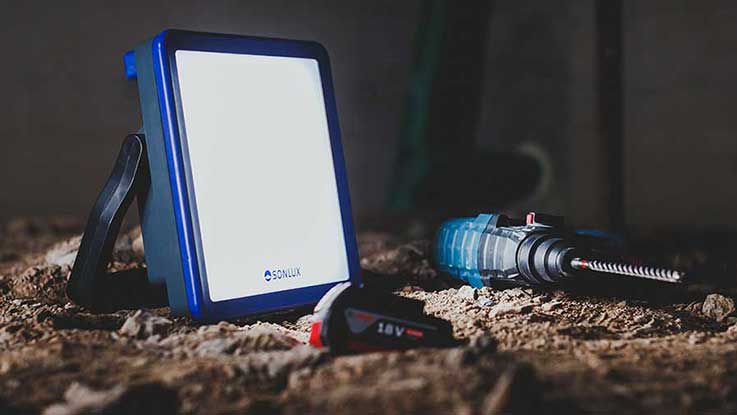 Modrý reflektor stojí na zemi vedle akumulátorového šroubováku.