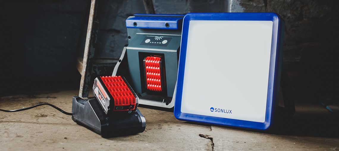 Červená baterie Bosch na černé nabíjecí stanici vedle reflektoru.