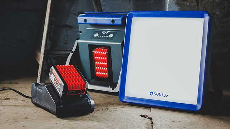 Červená nabíječka SONLUX stojí vedle bílého LED reflektoru.