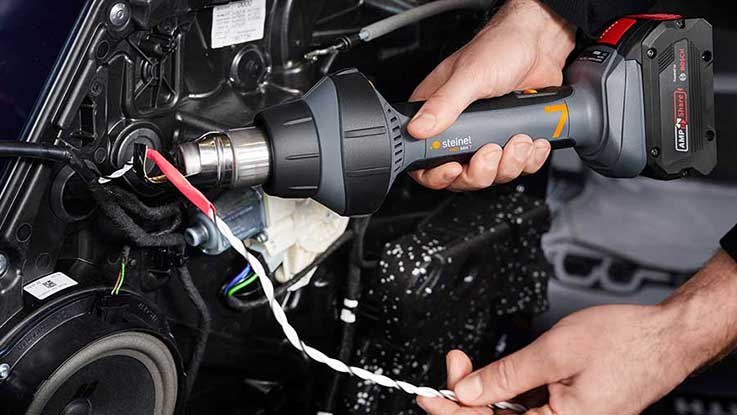 Šedý fén na vlasy s horkým vzduchem je držen u kabelového připojení.