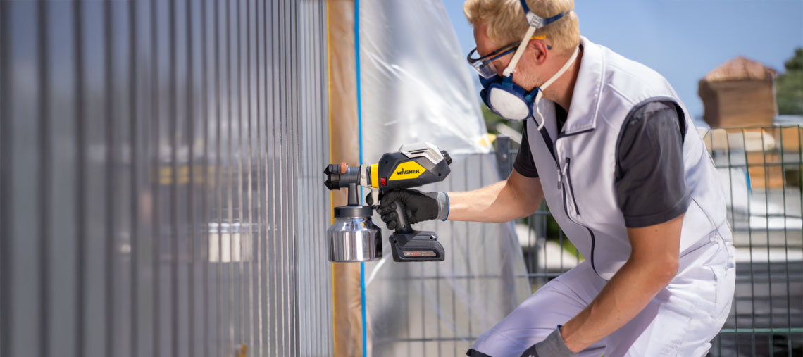 Řemeslník stříká zeď zařízením na malování Wagner.