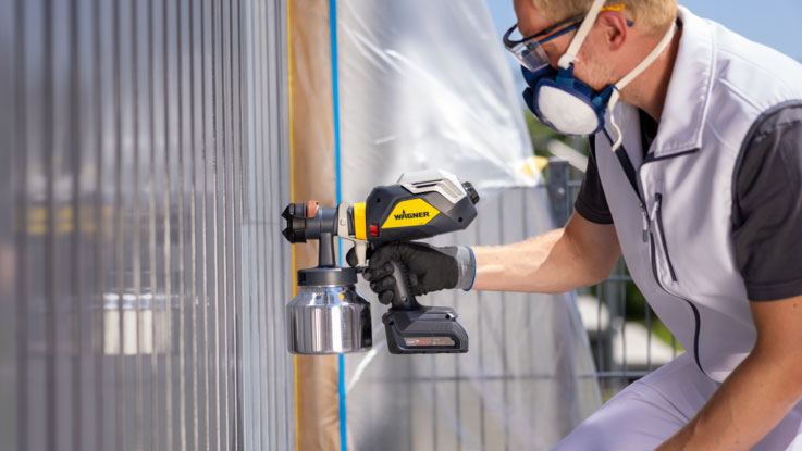 Řemeslník stříká barvu pomocí stříkací pistole Wagner na zeď.