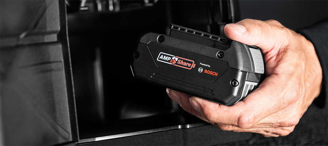 Ръка държи акумулатор Bosch AMPShare пред черен фон.