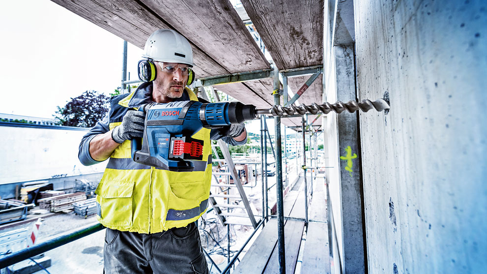 En arbejder med en Bosch boremaskine borer i en væg på stillads.