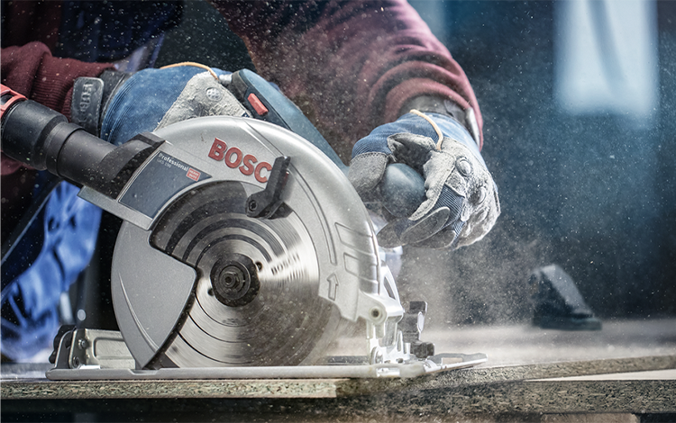 A Bosch Professional circular saw is cutting wood, dust is flying up.