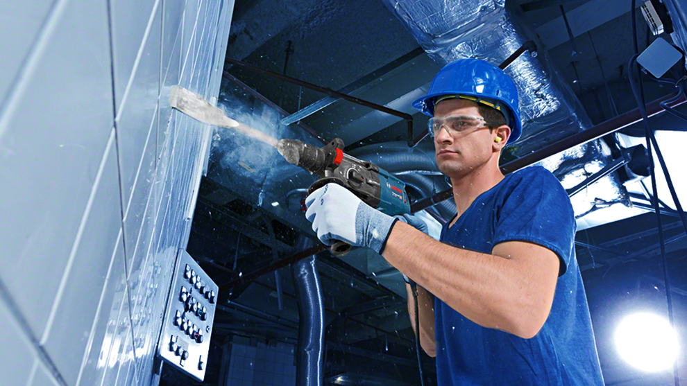 A man in blue clothing and a helmet is drilling into a wall with a Bosch tool.