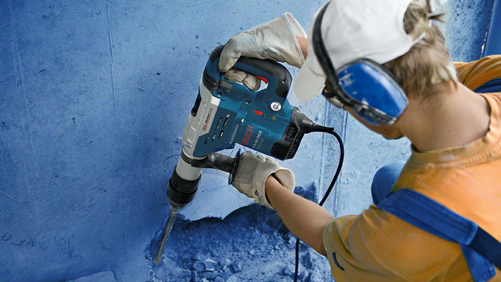 A worker is using a blue Bosch Professional drill on a wall.
