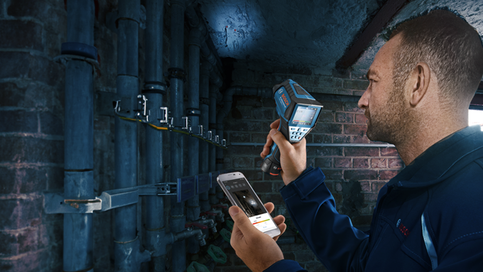 A technician uses a Bosch Professional measuring device and smartphone in a room.