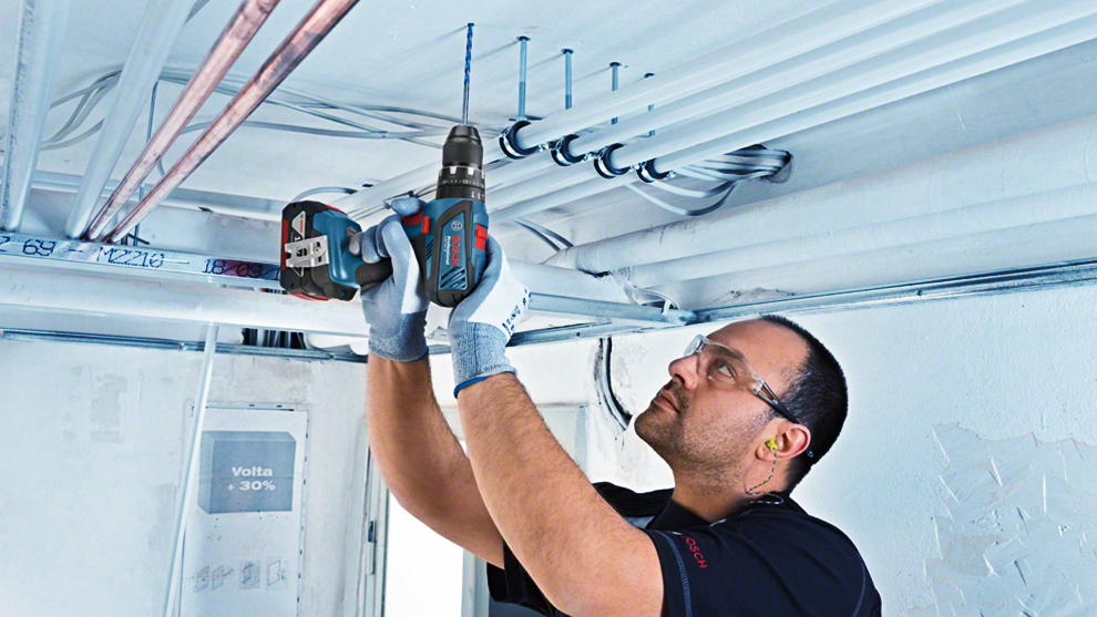 A man with a Bosch Professional cordless drill is installing pipes.