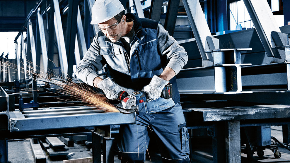 En arbetare med en Bosch vinkelslip bearbetar metallkomponenter i en verkstad.