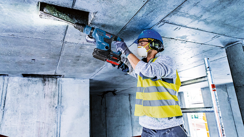 En arbetare med skyddshjälm borrar med ett blått Bosch Professional verktyg.