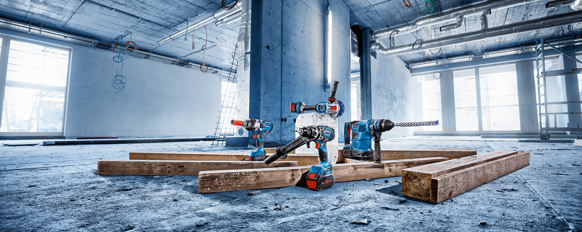 Four Bosch Professional tools are lying on wooden planks in the construction area.