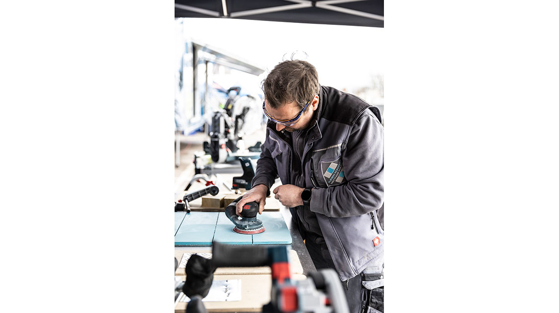 En håndværker bruger en Bosch slibemaskine på et bord.
