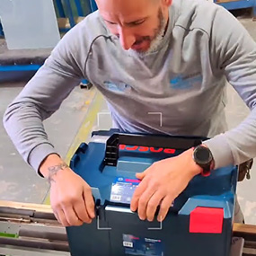 Un hombre abre una caja de herramientas azul Bosch Professional en un taller.