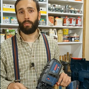 Un hombre con barba sostiene un clavador inalámbrico azul Bosch Professional en el taller.