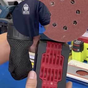 Una mano sostiene una lijadora Bosch con papel de lija rojo.