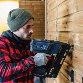 Un hombre con una camisa a cuadros está usando un clavador a batería en una pared de madera.