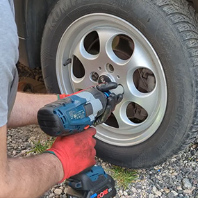 Un homme avec des gants bruts visse une roue en argent.