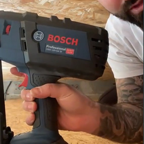Un artisan tient un cloueur sans fil bleu Bosch Professional.