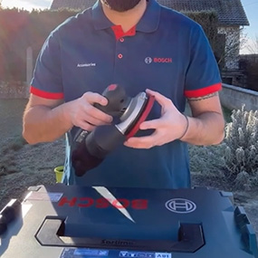 Un homme tient une meuleuse à batterie Bosch dans un jardin.