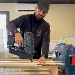 Un artisan utilise un cloueur à batterie Bosch bleu sur des planches de bois.