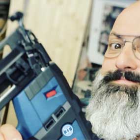 Un uomo con occhiali tiene un chiodatore a batteria blu Bosch Professional.