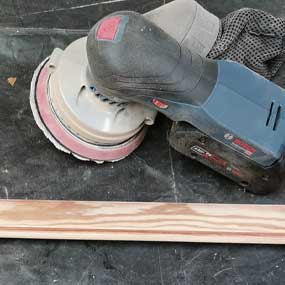 Un levigatore a batteria Bosch Professional blu è posato su una tavola di legno.