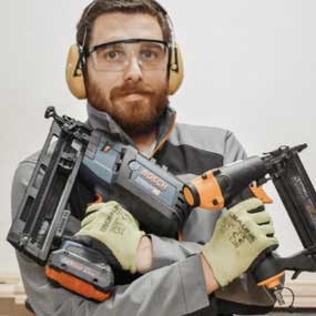 Um homem com óculos de proteção e protetores auriculares segura duas ferramentas Bosch Professional.