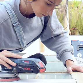 Uma mulher usa uma lixadeira a bateria Bosch Professional em madeira.