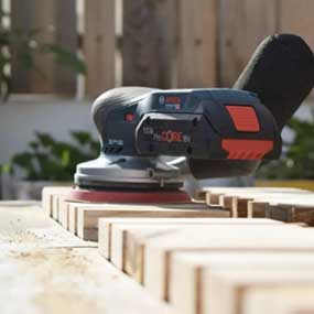 Uma lixadeira excêntrica preta Bosch Professional está em cima de tábuas de madeira.