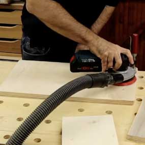Uma mão usa uma lixadeira orbital Bosch Professional em madeira.