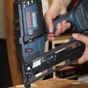 Uma mão segura um grampeador sem fio azul Bosch Professional sobre a madeira.